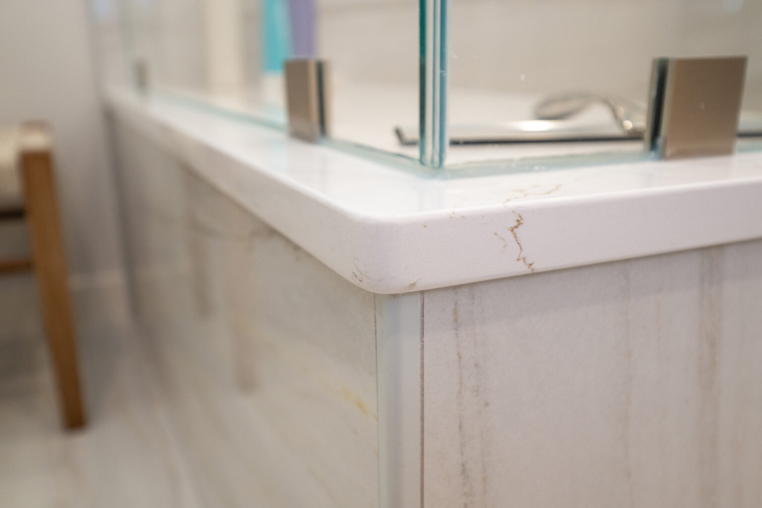 Close-up of a bathroom glass shower enclosure with metal brackets secured to a white polished marble edge, showing a small crack on the marble surface.
