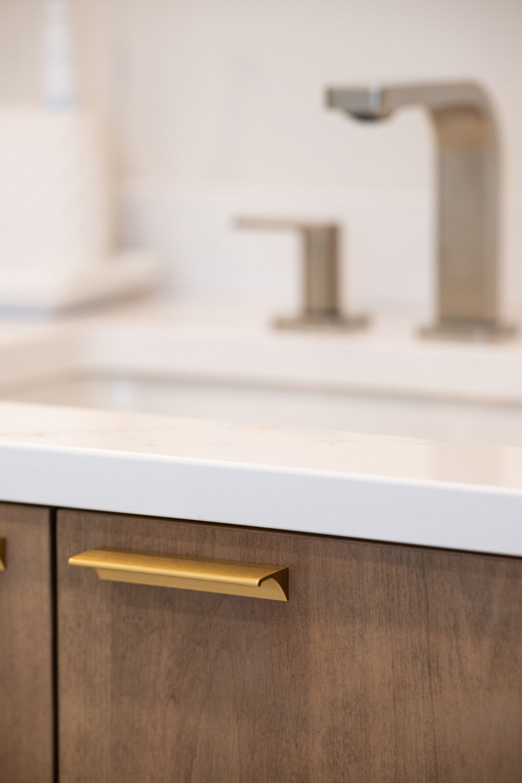 Close-up of a kitchen sink area with a modern faucet and soap dispenser on a white countertop, and wooden cabinets with a gold handle.