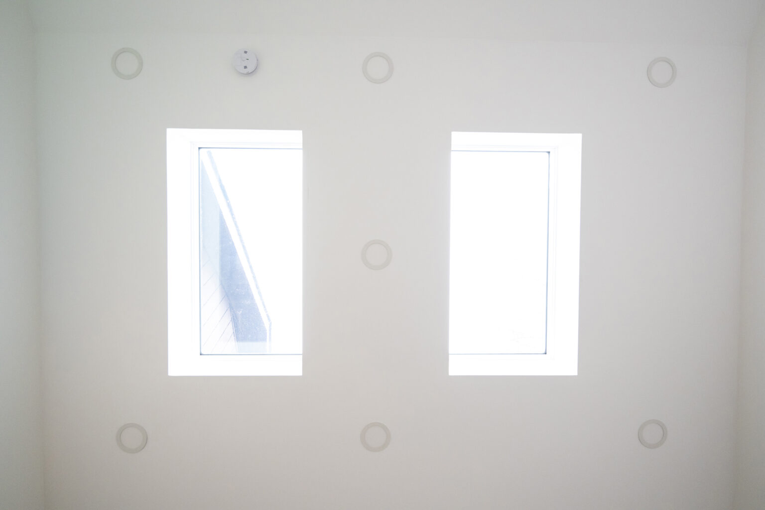 A white wall with two rectangular windows, each showing an exterior view of a building. Circular designs are spaced evenly around the windows.