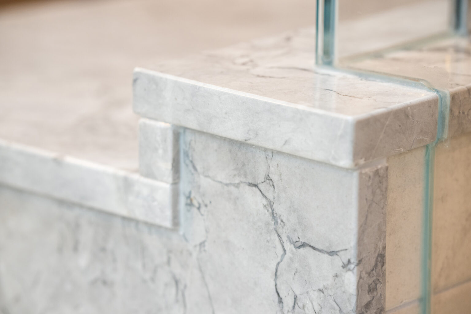 Image by Lesnick Photo Close-up image of a marble countertop with visible gray veining and a polished finish next to a glass barrier.