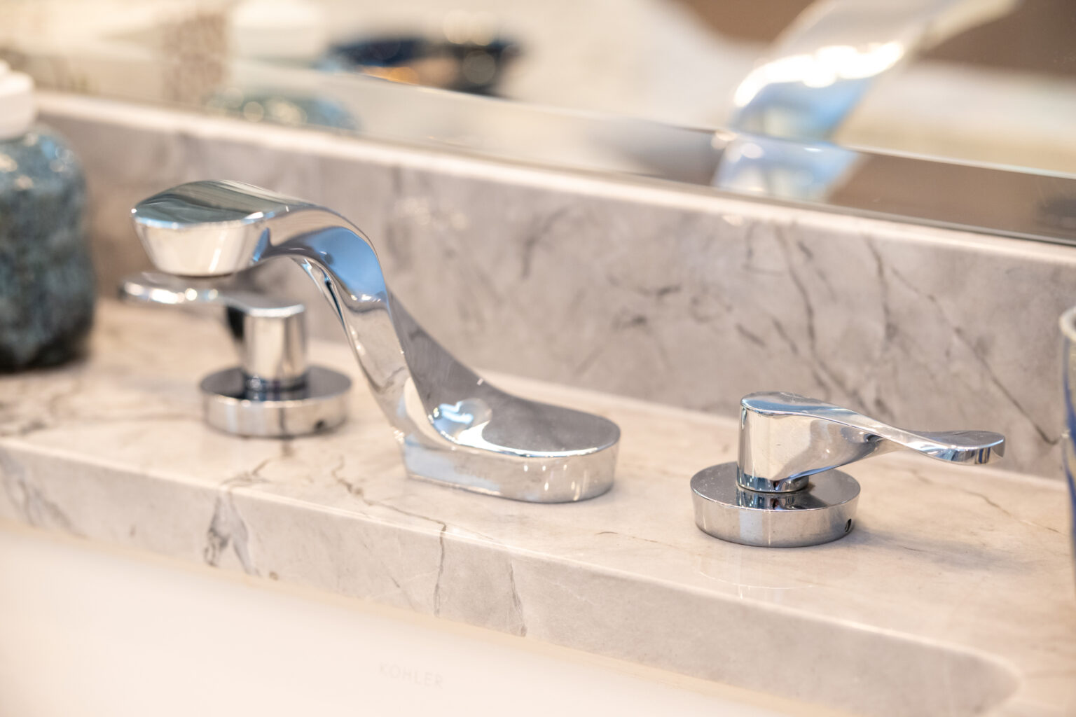 Image by Lesnick Photo Close-up of a modern, metallic bathroom sink faucet and tap handles mounted on a marble countertop.