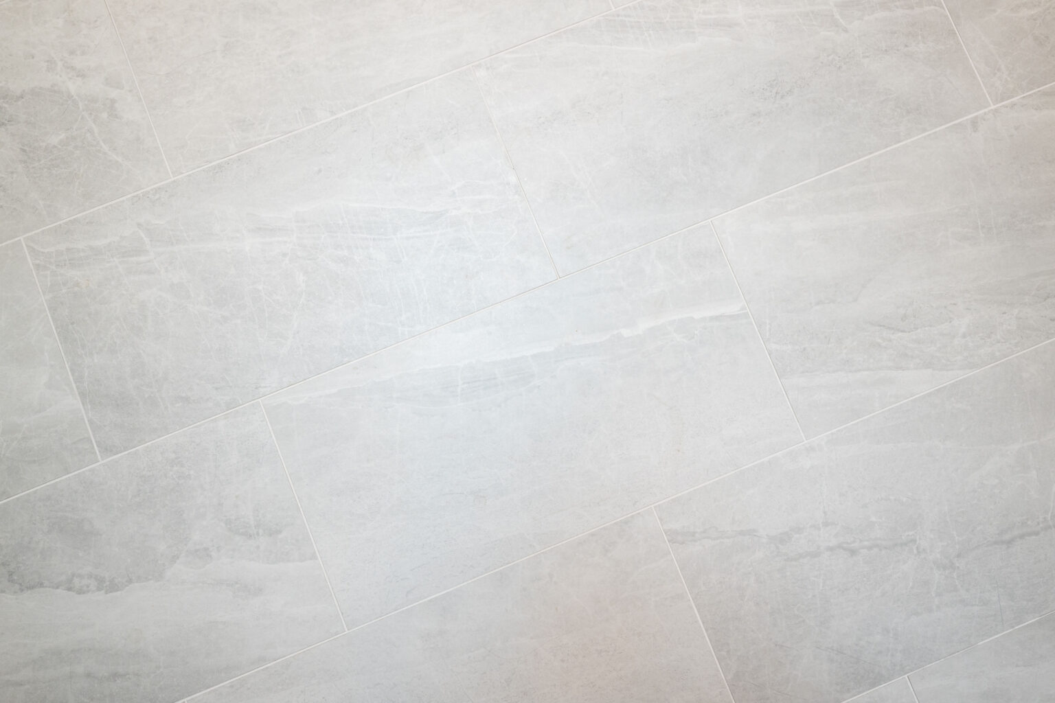 A close-up view of a light gray tiled floor with a subtle, marbled pattern. The tiles are rectangular and arranged in a staggered pattern.