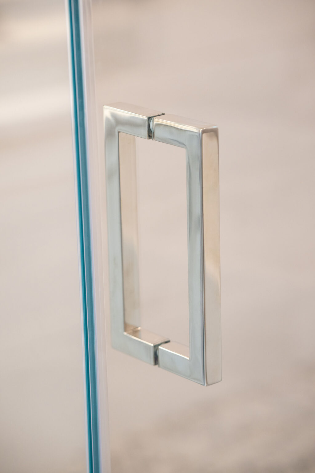 Close-up of a modern rectangular metal handle on a glass door with a blurred background.