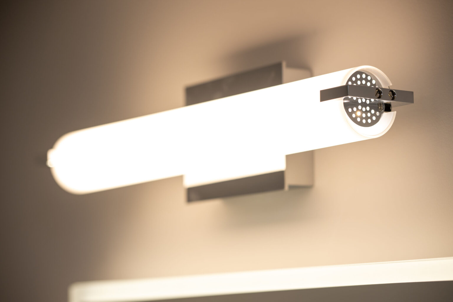 A wall-mounted LED light fixture with a frosted tube design illuminated against a beige background.