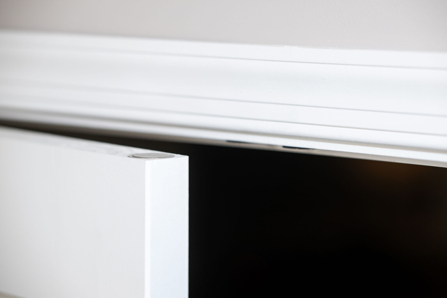 Close-up of a white door slightly ajar, with a white doorframe and light grey wall in the background.