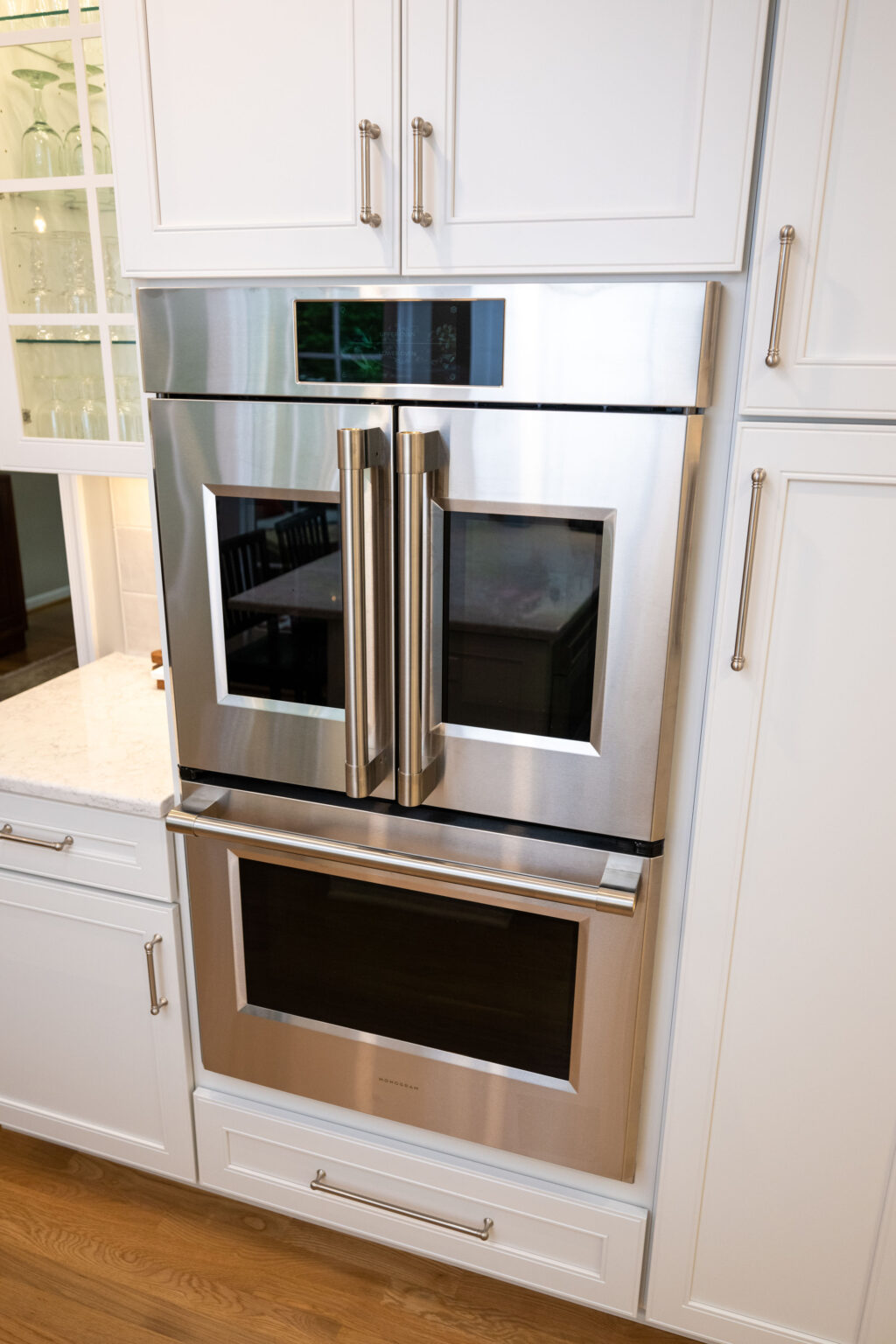 Image by Lesnick Photo A stainless steel built-in double oven with a French door upper oven and a traditional single door lower oven, integrated into white kitchen cabinetry.