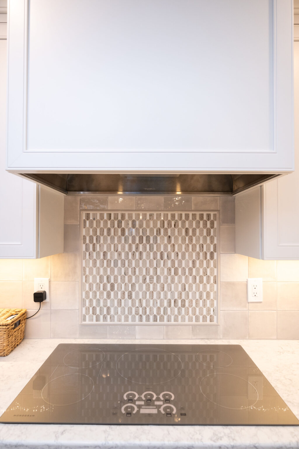 Image by Lesnick Photo A modern kitchen features a glass-ceramic induction cooktop beneath a stainless steel range hood and a mosaic tile backsplash.