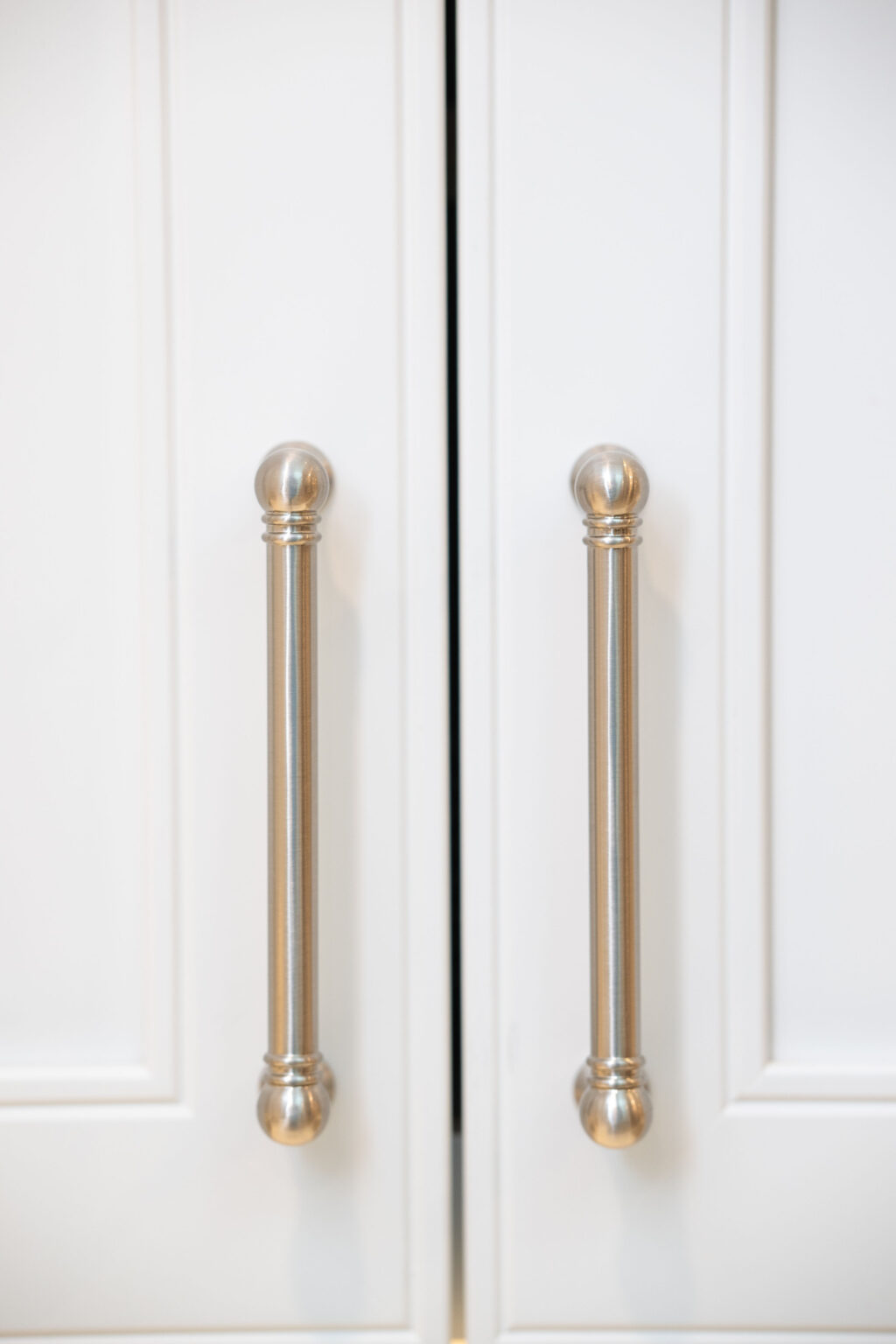 Image by Lesnick Photo Two silver metal cabinet handles are mounted on white cabinet doors.