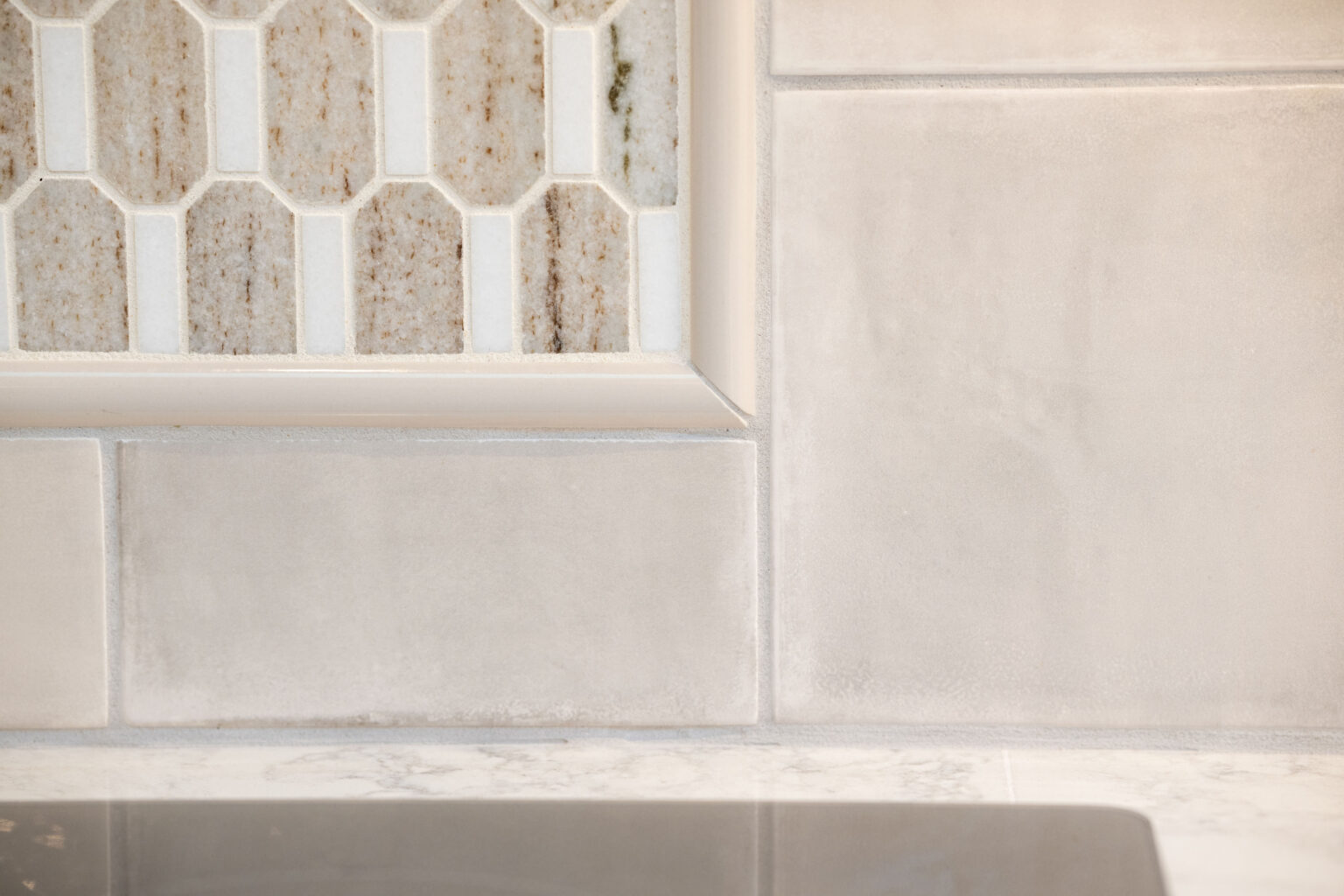 Image by Lesnick Photo Close-up of kitchen backsplash showing two different tile patterns: hexagonal tiles on the left and rectangular tiles on the right, above a countertop.
