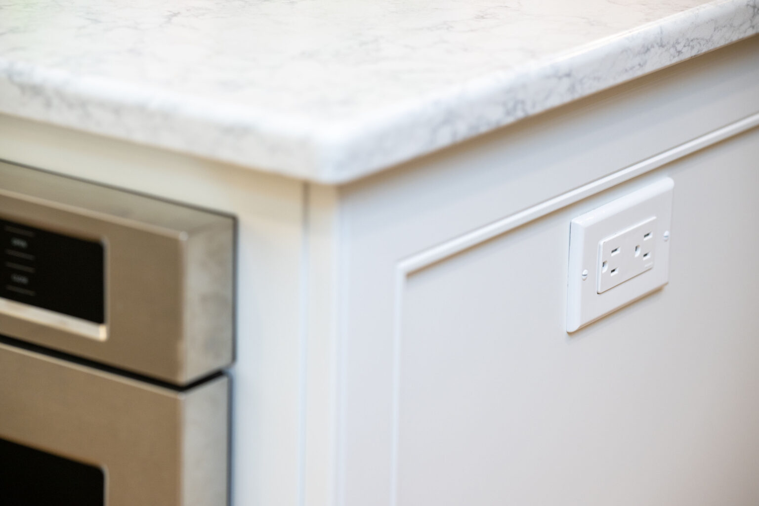Image by Lesnick Photo A close-up of a white kitchen countertop with an integrated oven on the left and an electrical outlet on the side of the cabinet.