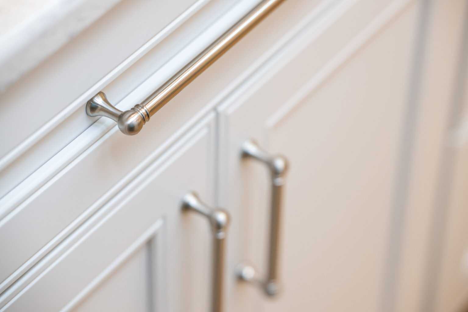 Image by Lesnick Photo Close-up of white kitchen cabinets with silver handles and a countertop edge visible at the top left.