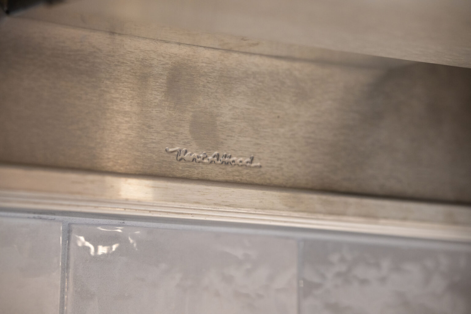 Image by Lesnick Photo The image shows a metallic surface engraved with the word "KitchenAid" above a row of glossy, textured white tiles.