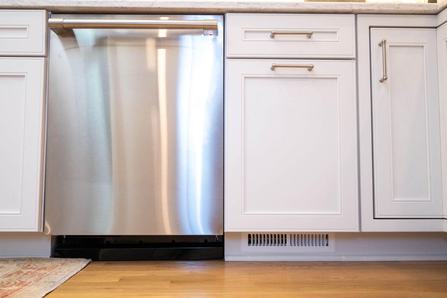 Image by Lesnick Photo A stainless steel dishwasher is installed between white cabinets under a marbled countertop in a kitchen.