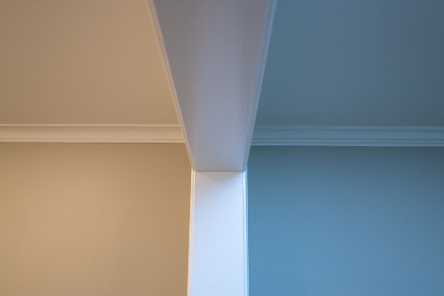 Image by Lesnick Photo A ceiling corner with a white beam dividing the space, the wall on one side is beige, and the wall on the other side is light blue.
