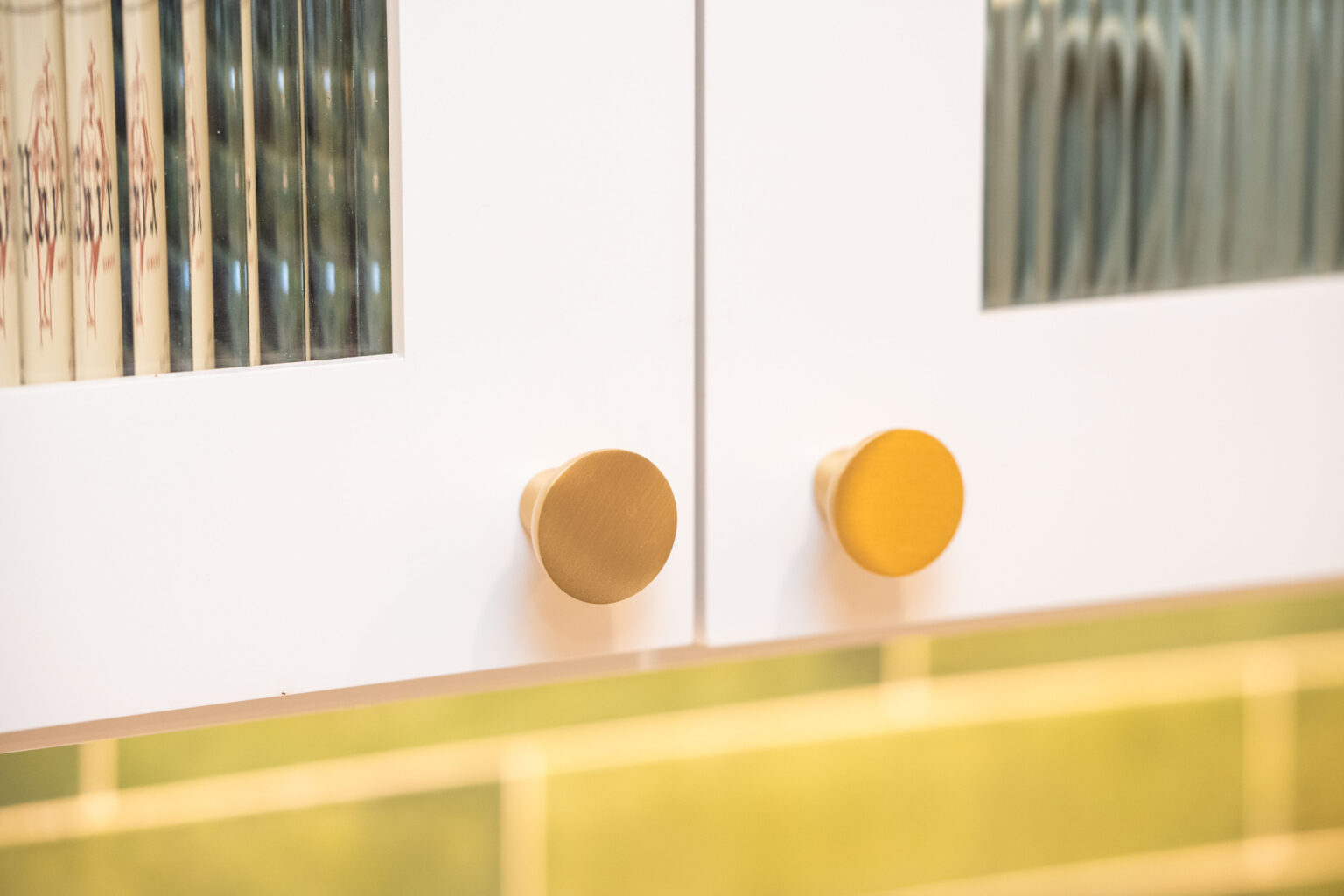 Image by Lesnick Photo Close-up of two white cabinet doors with round brass knobs and glass detailing.