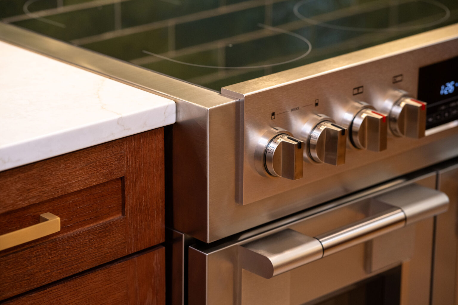 Image by Lesnick Photo Close-up of a modern stainless steel oven with four control knobs next to a wooden cabinet with a brass handle.