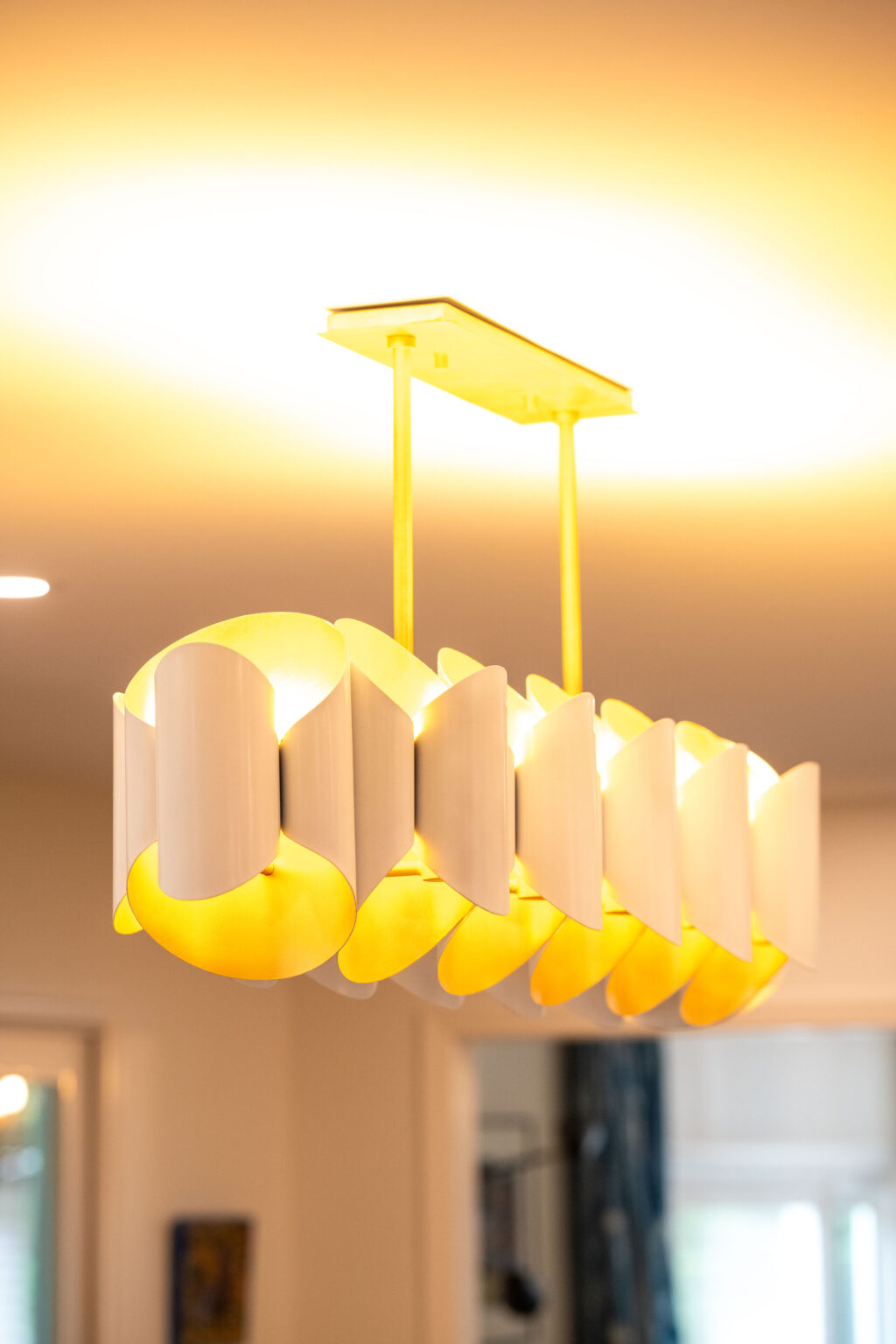 Image by Lesnick Photo A modern chandelier with geometric, white and gold panels emits a warm glow.