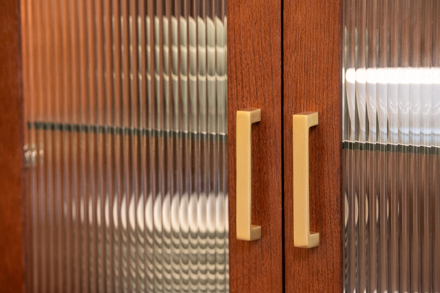 Image by Lesnick Photo Close-up of wooden cabinet doors with vertical glass panels and beige handles.