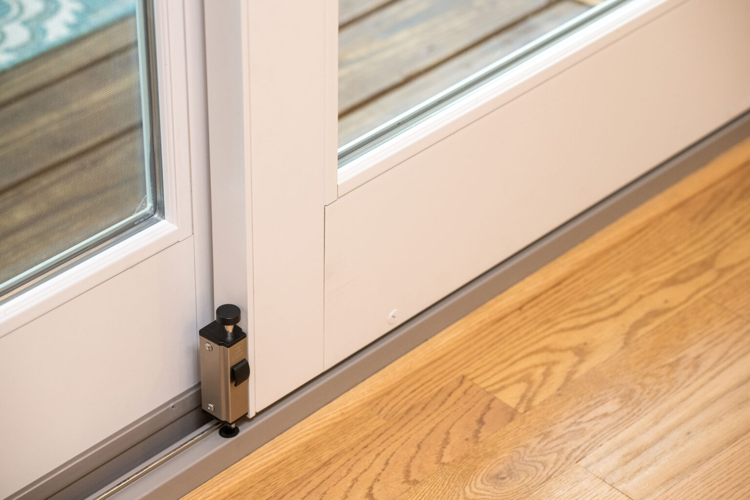 Image by Lesnick Photo A sliding glass door with a security bolt lock installed at the bottom, set against a wooden floor.