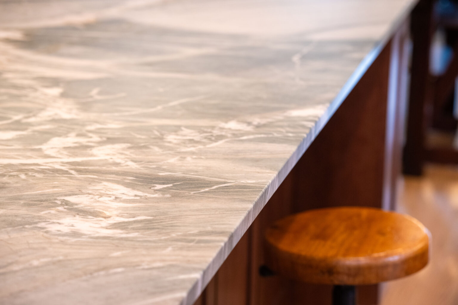 Image by Lesnick Photo Close-up of a polished granite countertop with shades of gray and white, above a wooden stool.