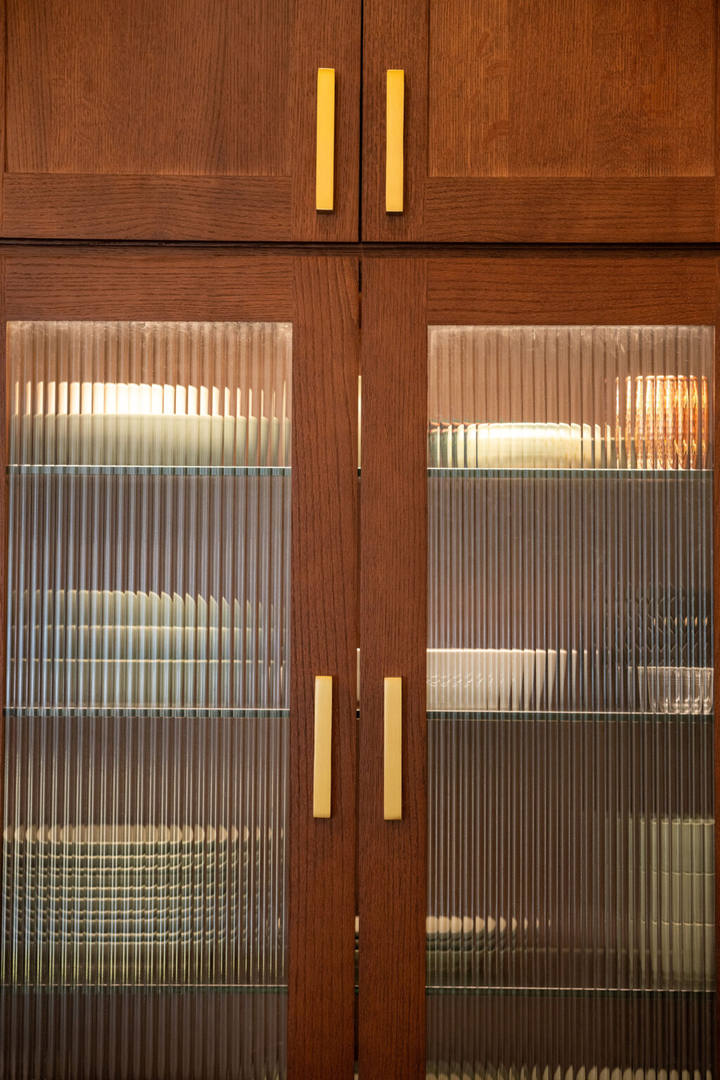 Image by Lesnick Photo Wooden cabinet with ribbed glass doors; inside are stacked white plates and bowls.