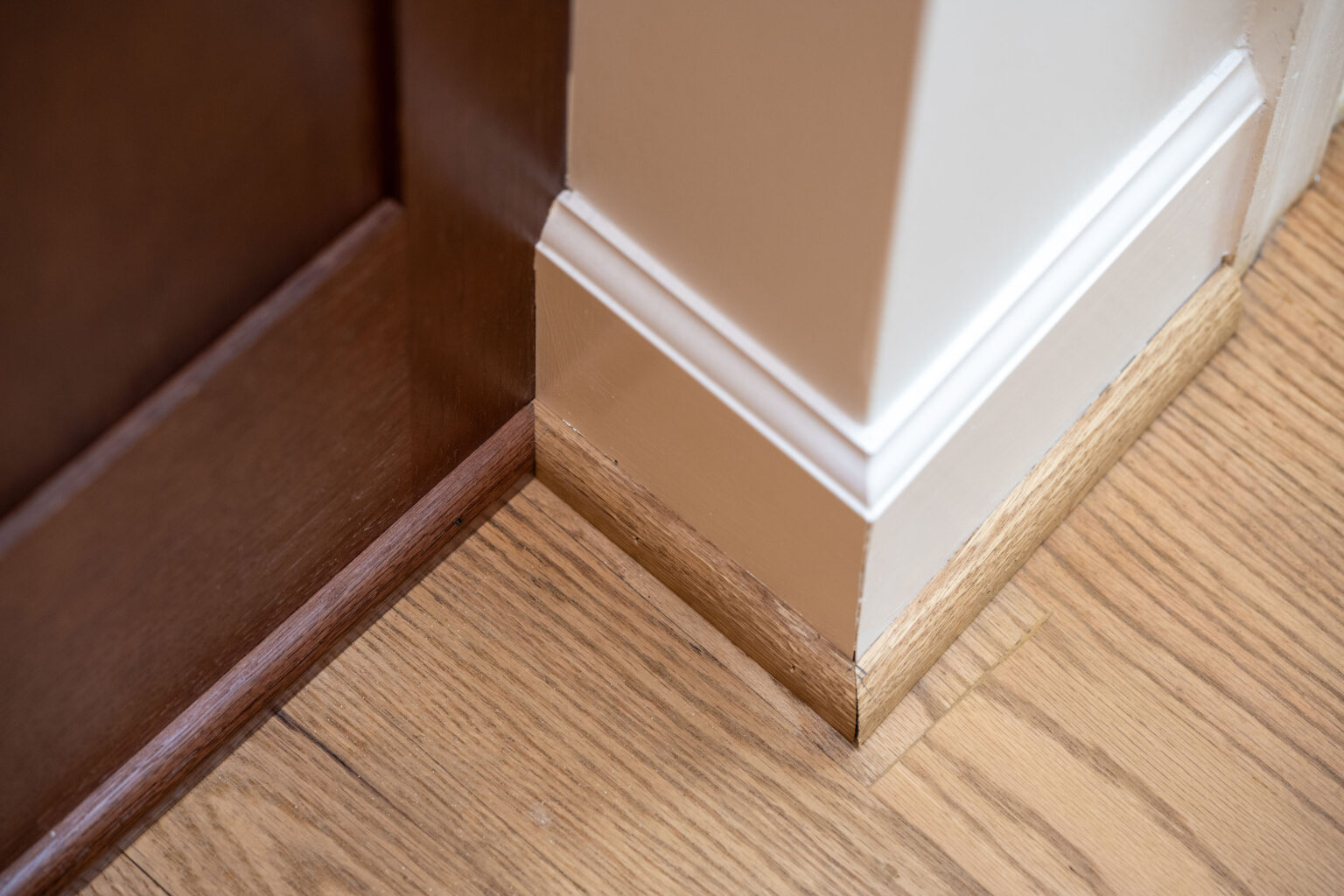 Image by Lesnick Photo A wooden floor meets a white wall with a brown door. The floor has a natural wood grain, and the wall features a baseboard trim. The door is slightly ajar.