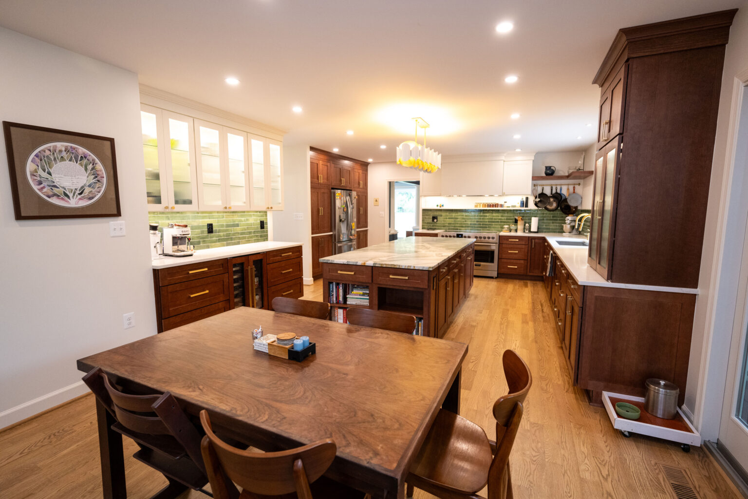 Image by Lesnick Photo Modern kitchen with wooden cabinets and flooring, featuring a center island with stools and a dining table with chairs. Bright lighting and art on the wall enhance the room's warm ambiance.