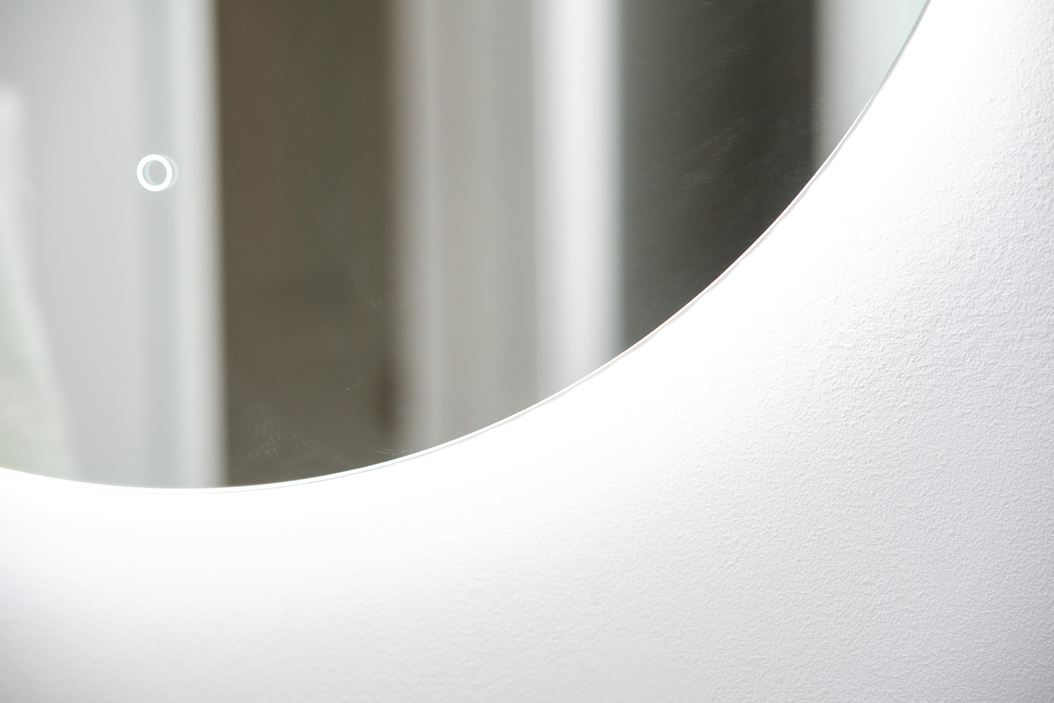 Close-up of a round mirror with a visible touch button on the left side, reflecting a blurred background. The frame is white and the surface is smooth.