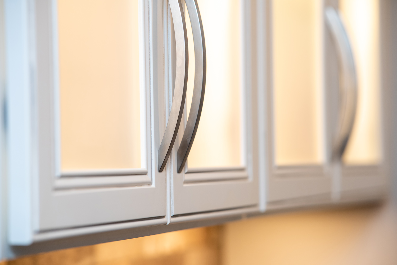 Close-up of white kitchen cabinets with silver handles, shown under warm lighting.