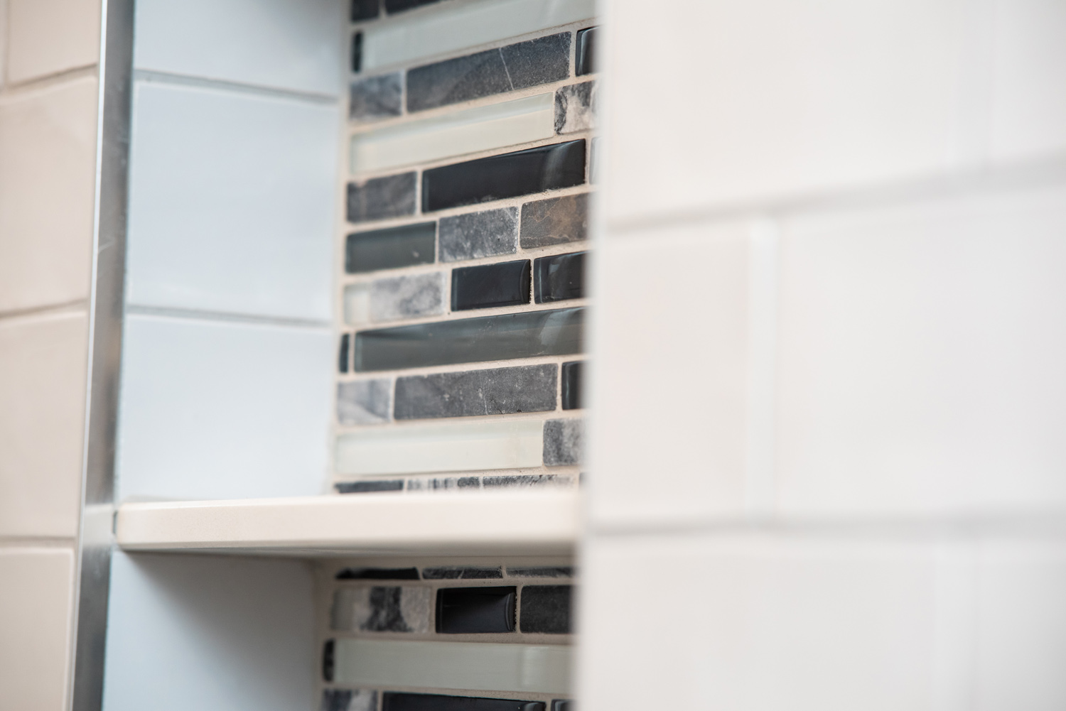 Close-up of a wall with a shelf, featuring a mix of cream, black, and blue rectangular tiles.