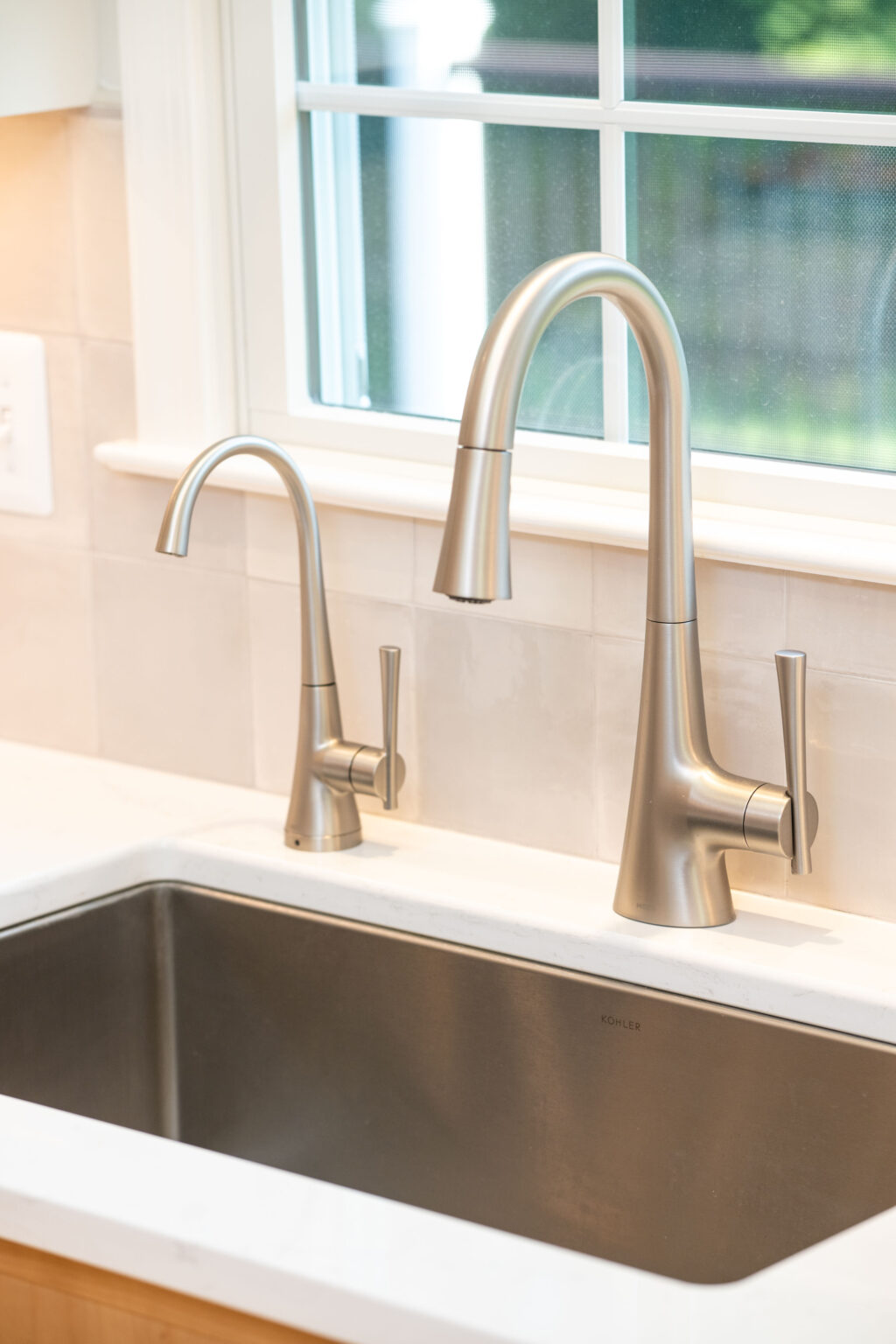 A modern kitchen sink with stainless steel faucets and a window in the background.