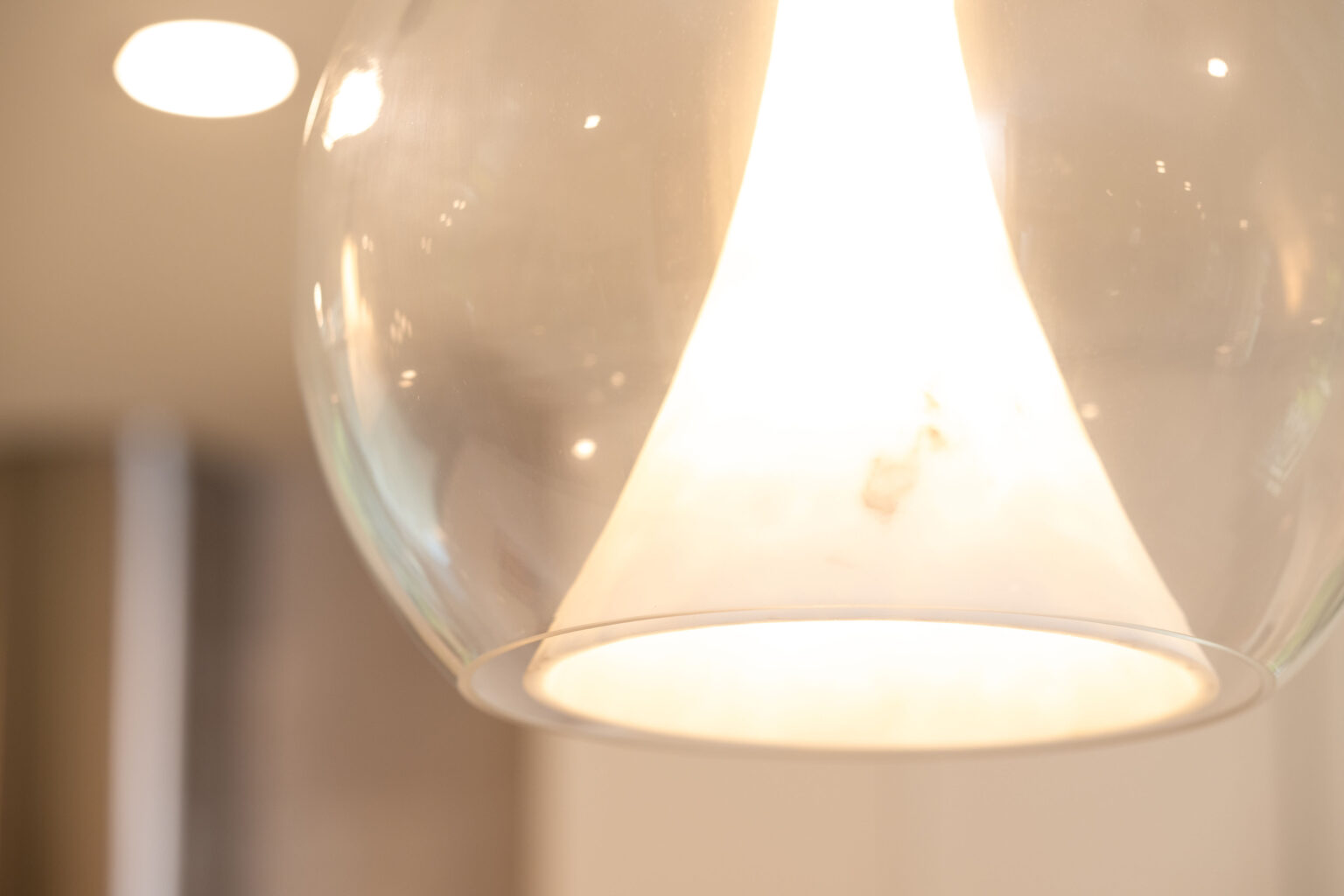 A close-up view of a lit pendant lamp with a clear glass shade, emitting a warm light.