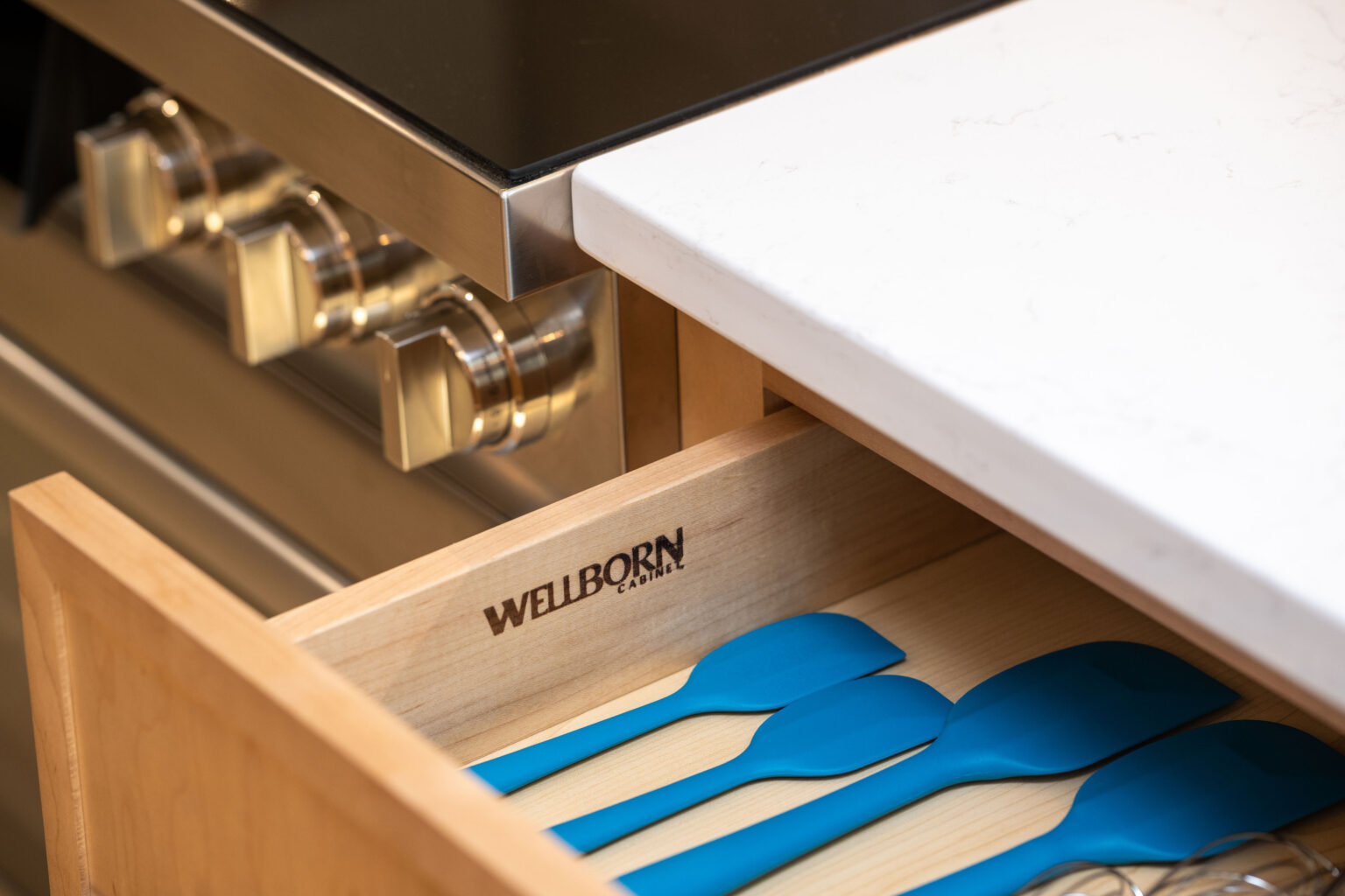 Open kitchen drawer with blue spatulas next to a stainless steel stove.
