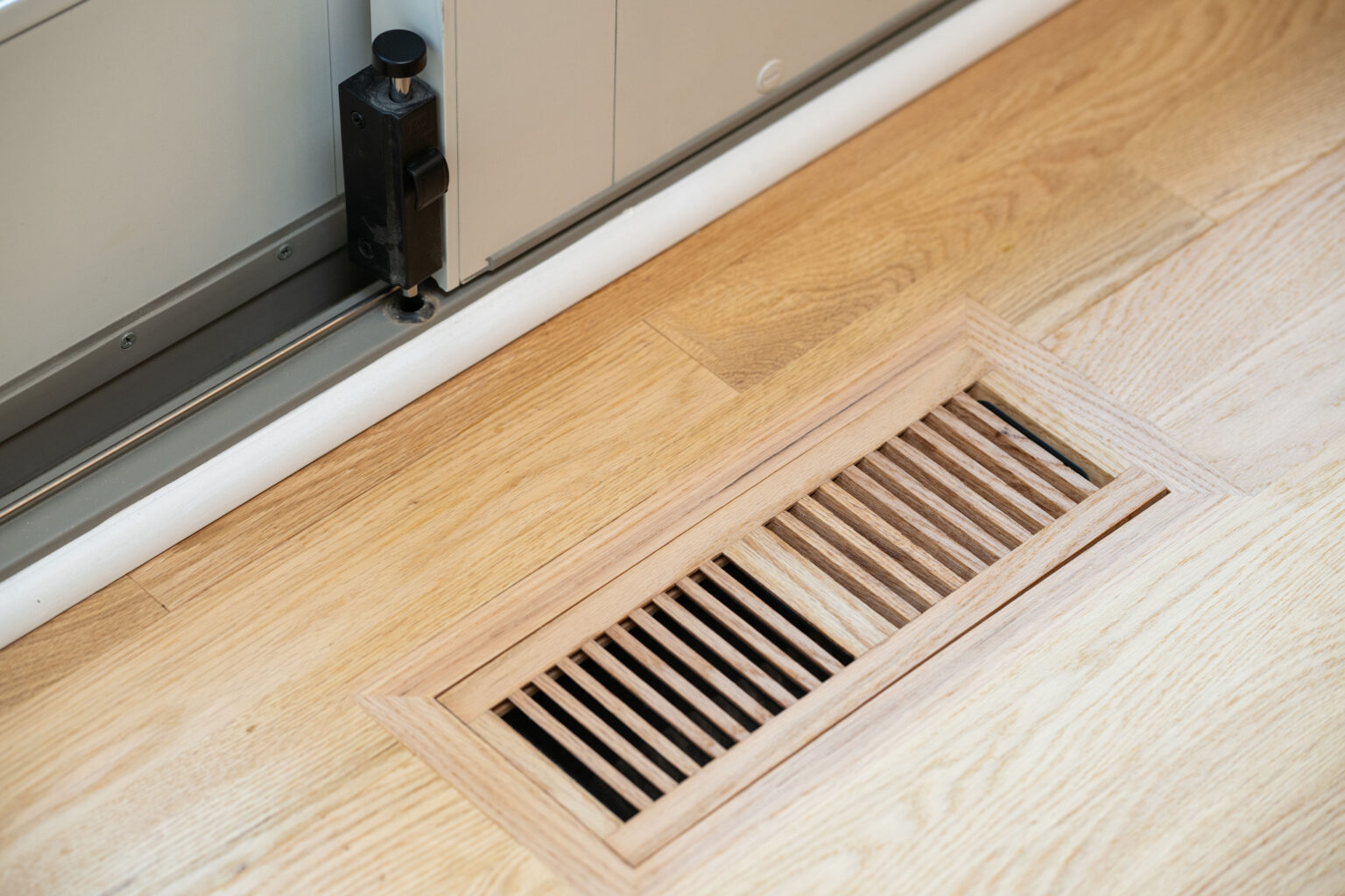 Wooden floor vent near a metal sliding door.