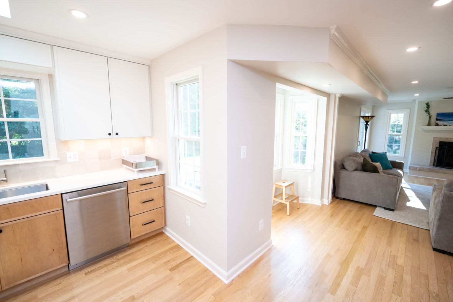 Bright, open kitchen and living area with wood floors, white walls, modern cabinets, and a fireplace in the background.