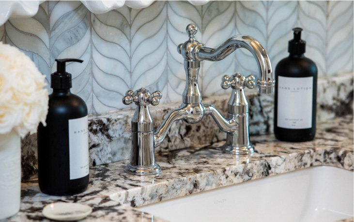 A polished chrome faucet on a granite bathroom countertop, flanked by two black pump bottles.