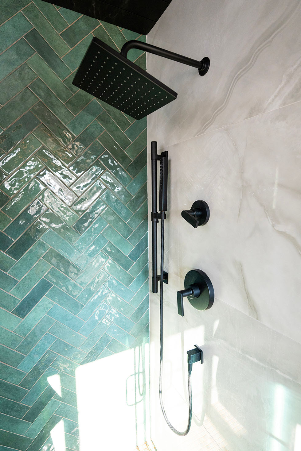 Modern shower with a large square rain showerhead and handheld attachment. Green herringbone tiles cover one wall, while the other wall is light-colored, offering a sleek style perfect for bathroom remodeling in Northern Virginia.
