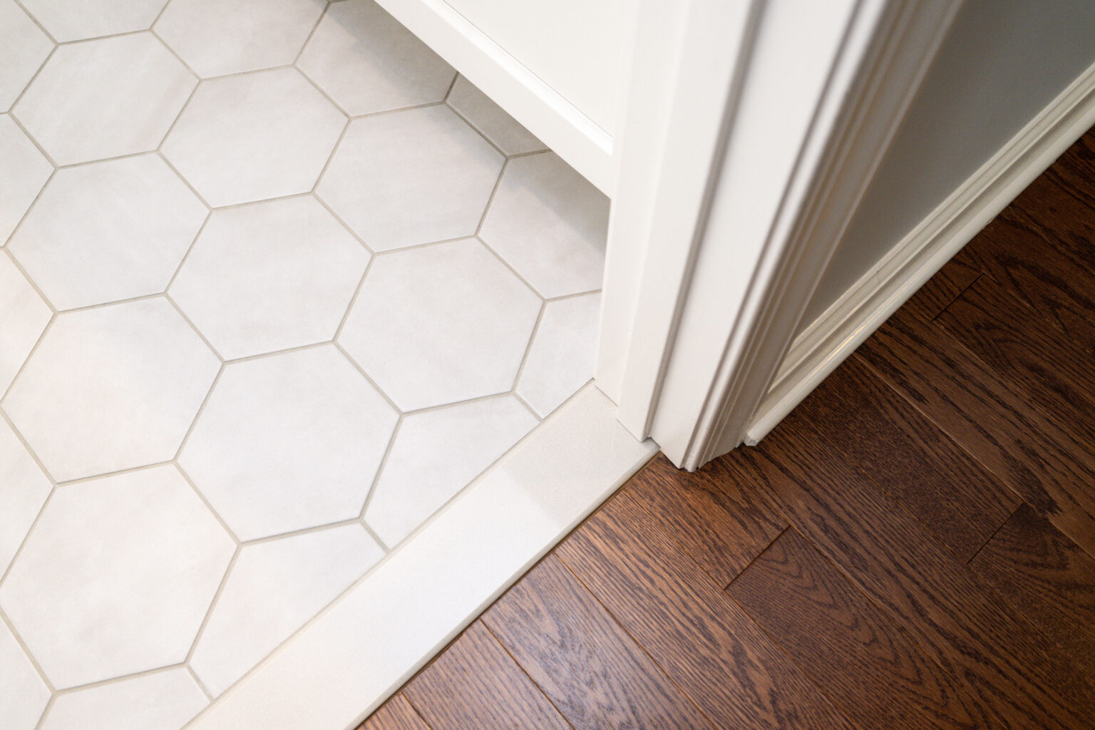 Image by Lesnick Photo Hexagonal white tiles transition to dark brown hardwood flooring at the threshold of a room.