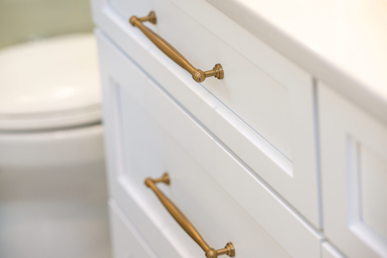 Image by Lesnick Photo Close-up of two white cabinet drawers with long, gold handles.