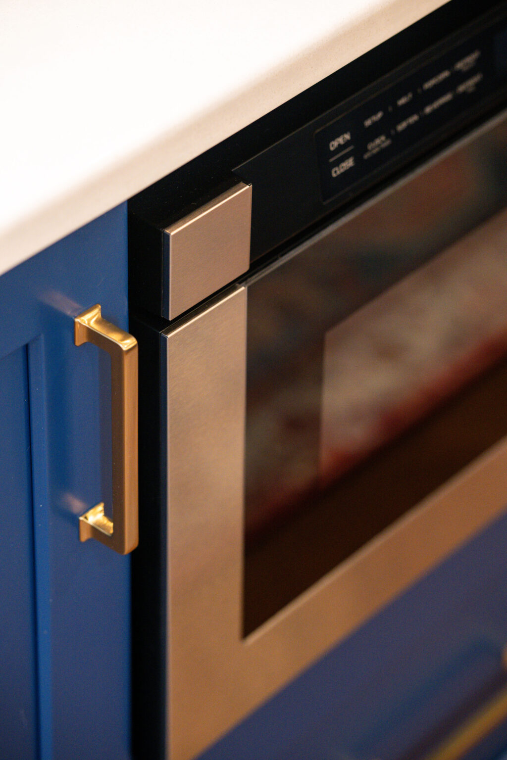 Image by Lesnick Photo Close-up of a stainless steel microwave with a digital display and handle on a blue cabinet.
