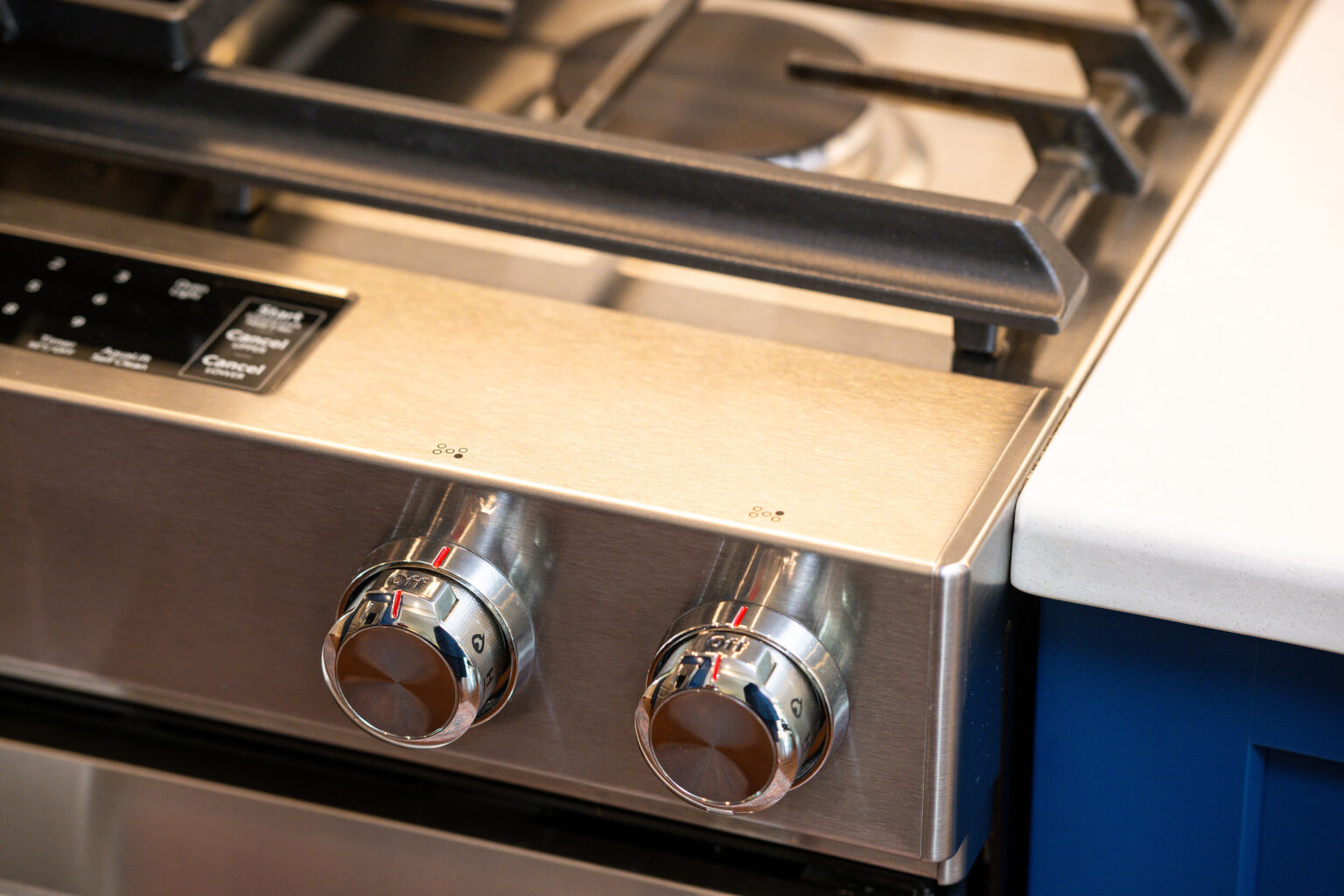 Image by Lesnick Photo Close-up of two stainless steel control knobs on a gas stove with a digital display panel, next to a countertop.