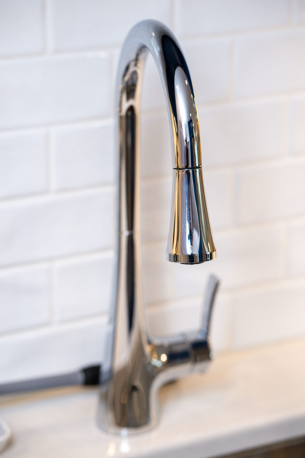 Image by Lesnick Photo A modern chrome kitchen faucet against a white tiled backsplash.