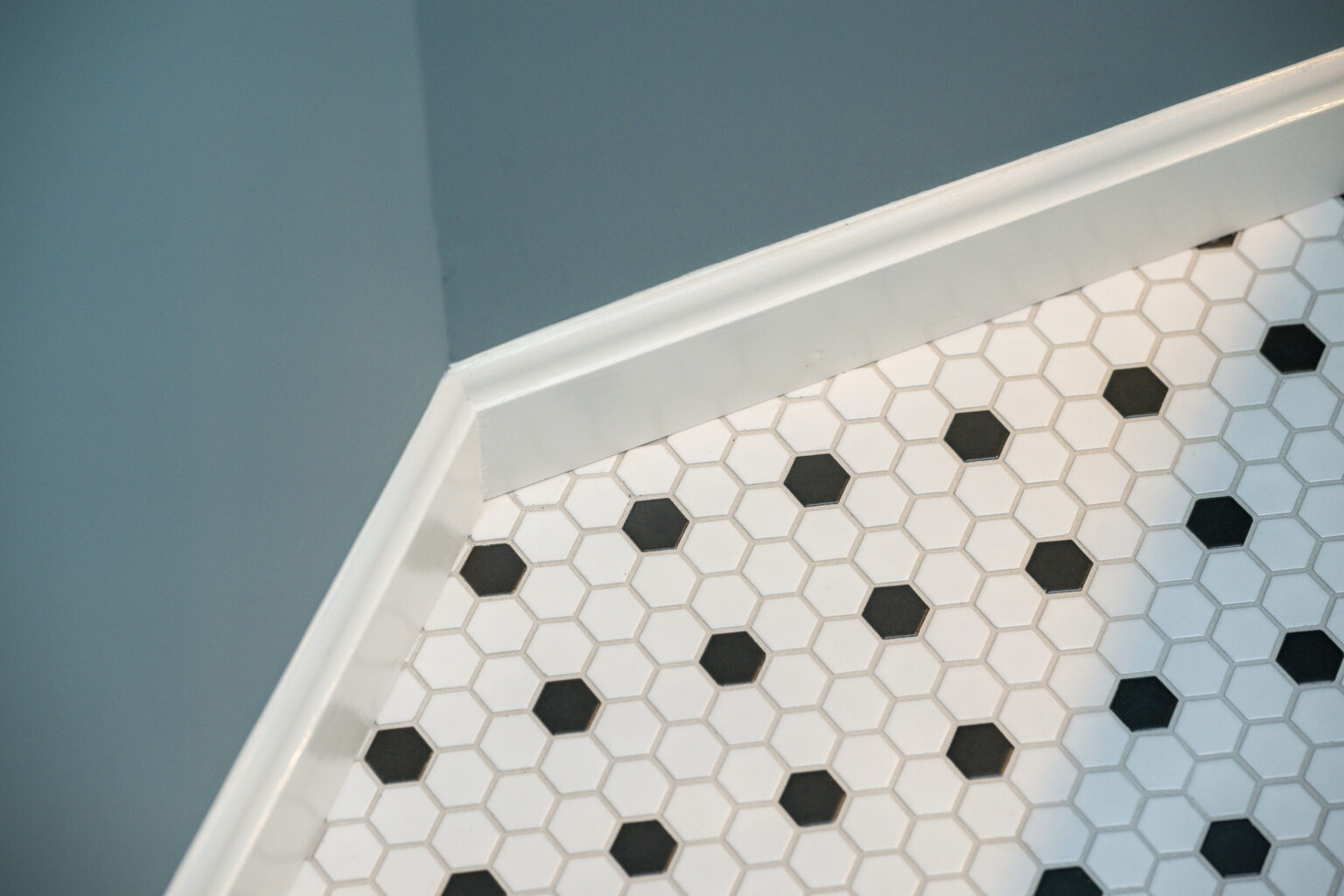 Image by Lesnick Photo Hexagonal black and white tiled floor with white trim against a gray wall corner.