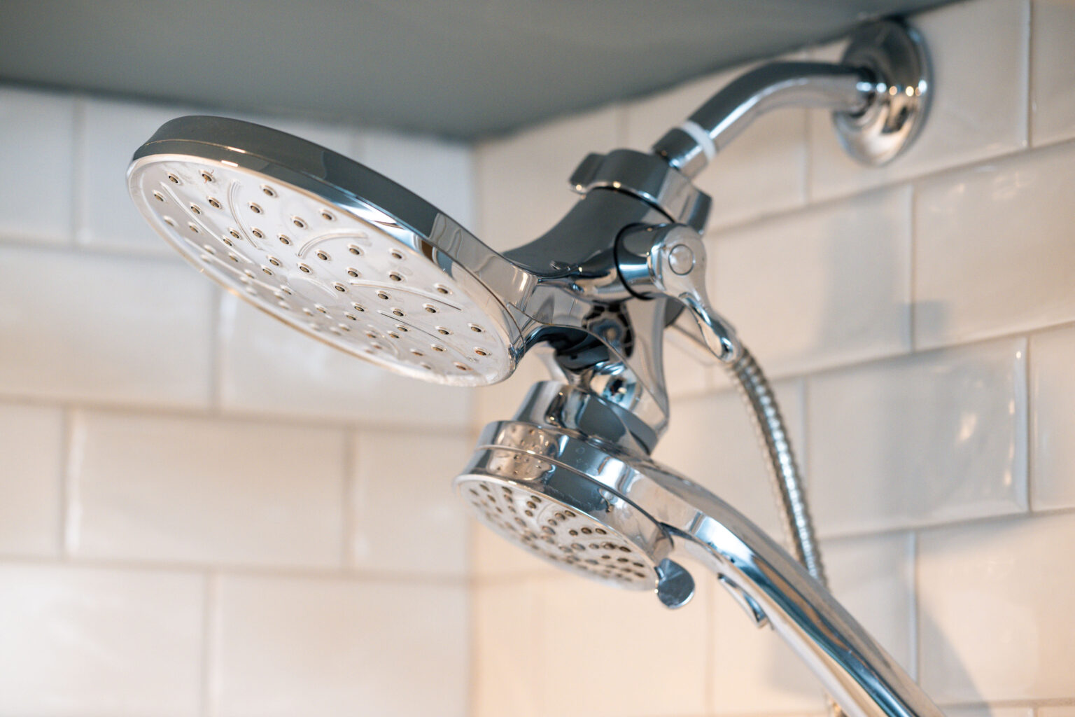 Image by Lesnick Photo Dual shower heads mounted on a white tiled wall, with a metallic finish and adjustable nozzles.