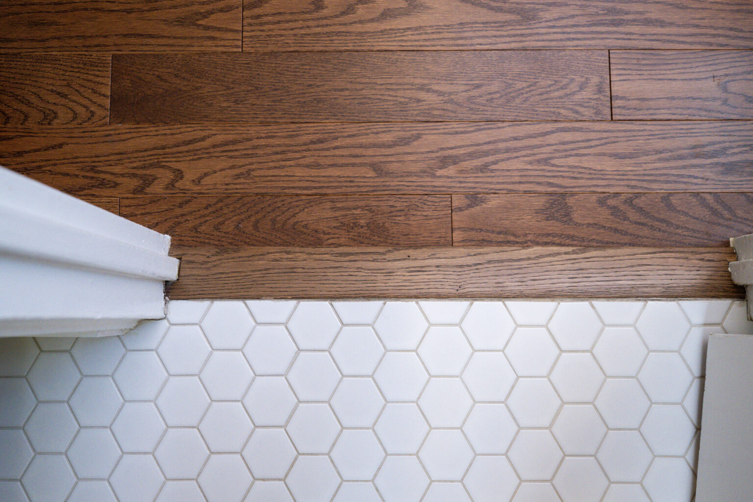 Image by Lesnick Photo A transition between hexagonal white tile flooring and brown wood flooring, with a wooden threshold in between.