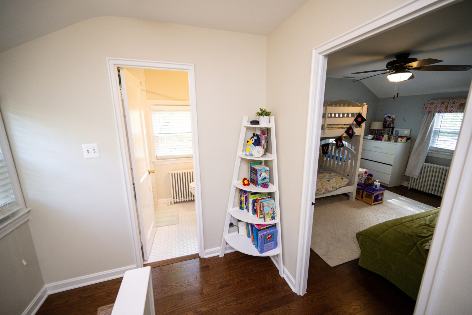 Image by Lesnick Photo Hallway with a white bookshelf, leading to a bathroom on the left and a children's bedroom with a bunk bed on the right.