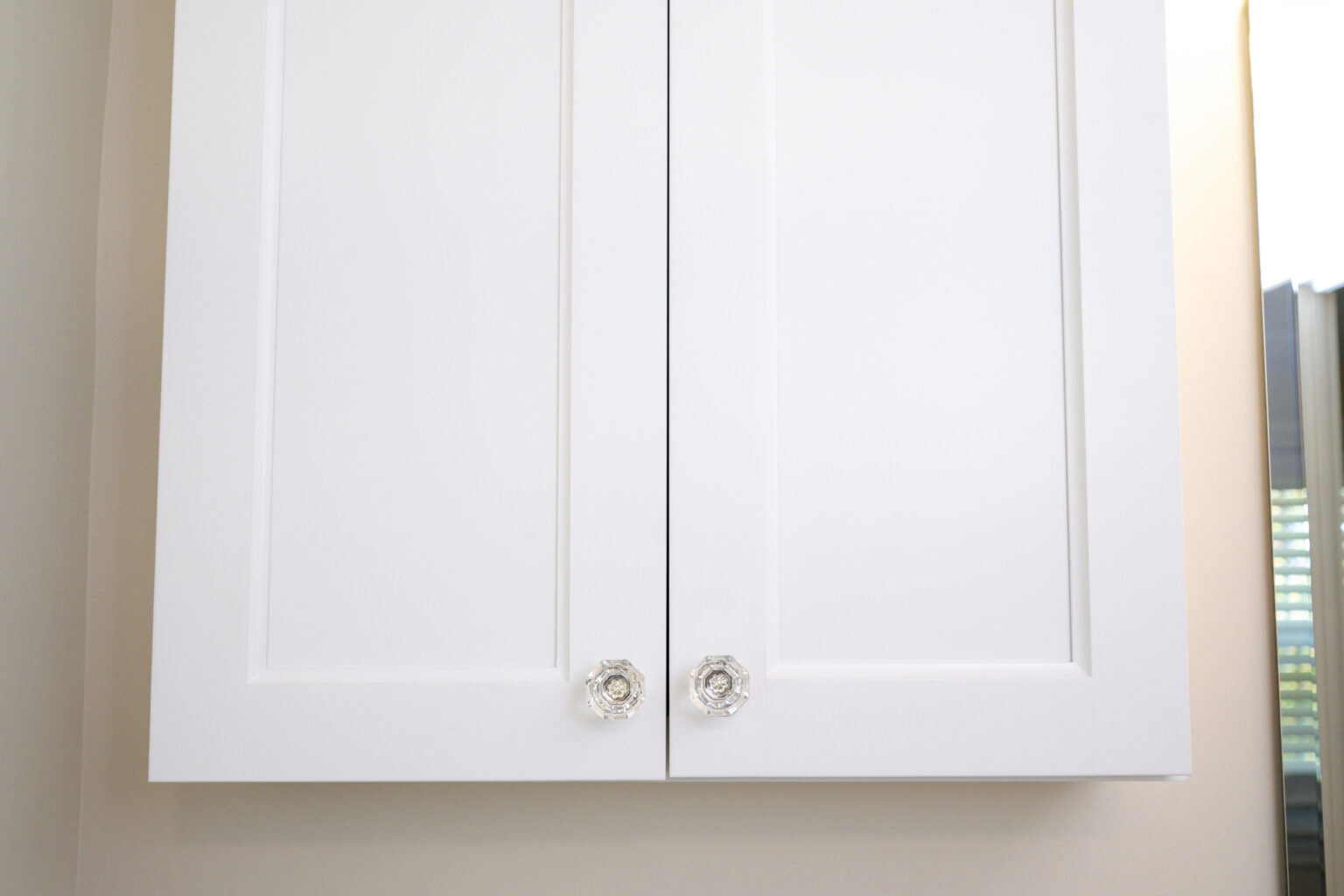 Image by Lesnick Photo White cabinet with two closed doors, each featuring a clear, round knob.