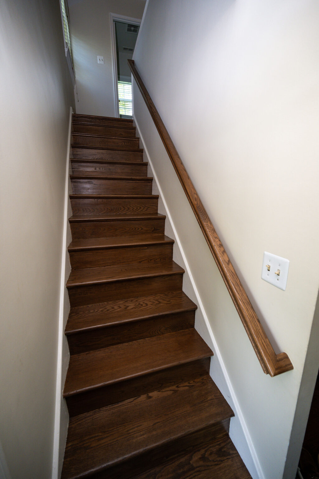 Image by Lesnick Photo Wooden staircase with a handrail on the right, leading to an open doorway at the top. Light switches are mounted on the right wall.