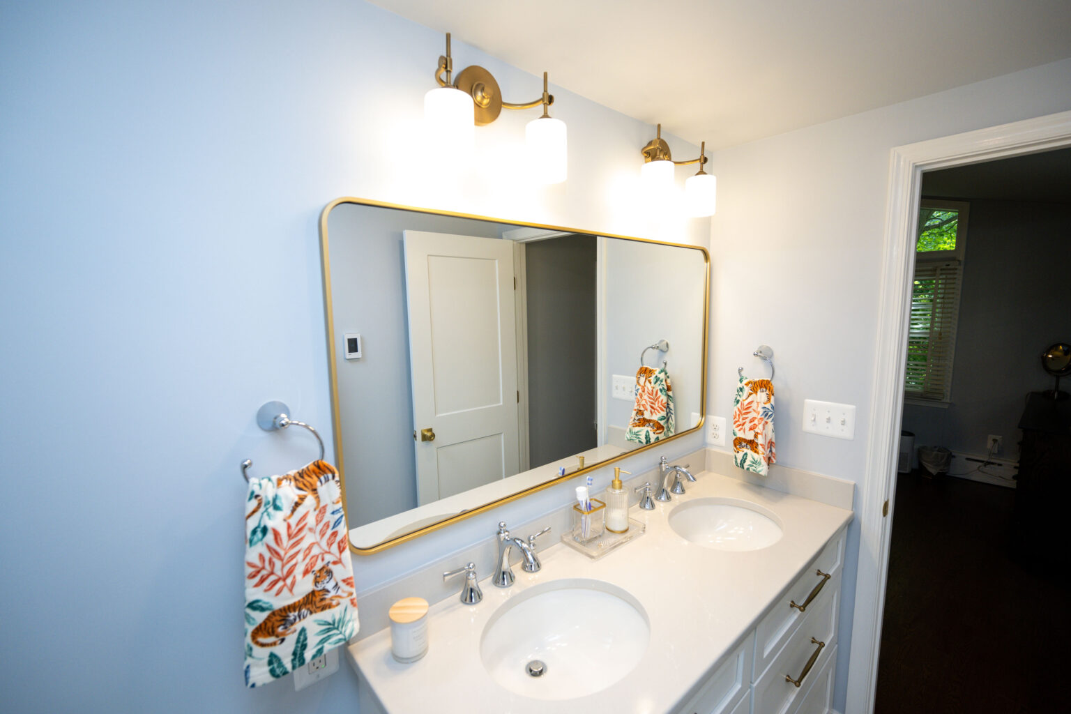 Image by Lesnick Photo Modern bathroom with a large mirror above a double sink vanity, featuring floral hand towels and wall-mounted lights.