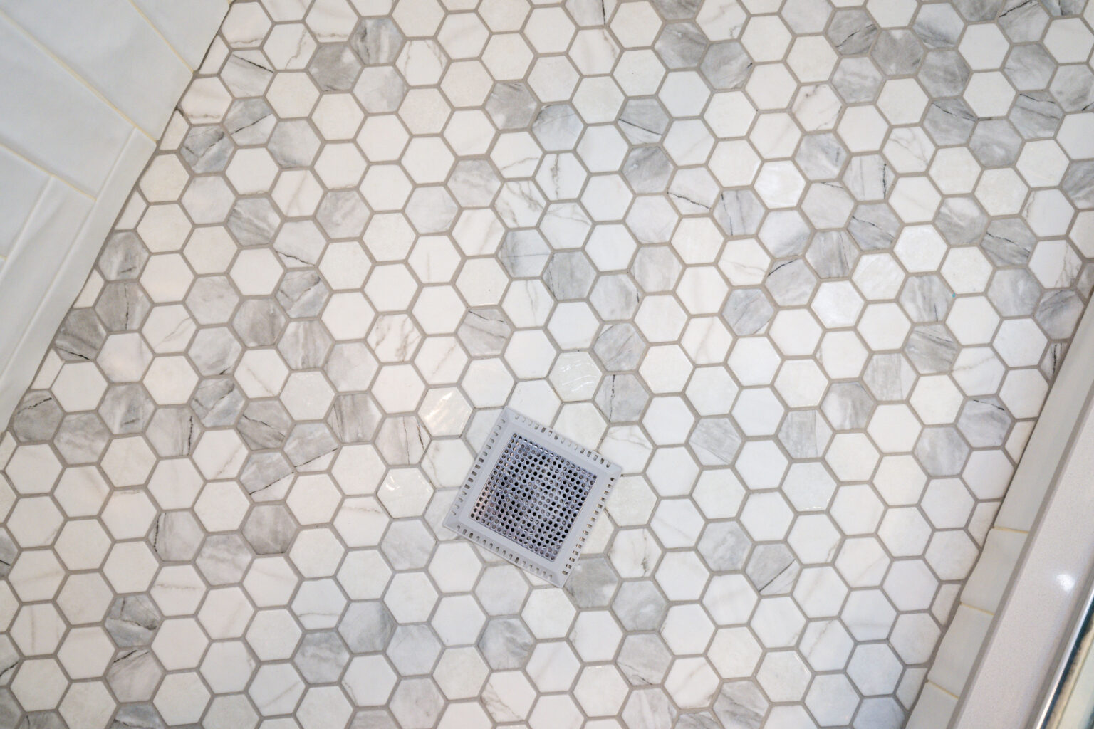 Image by Lesnick Photo Hexagonal tile floor in a shower with a central square metal drain.